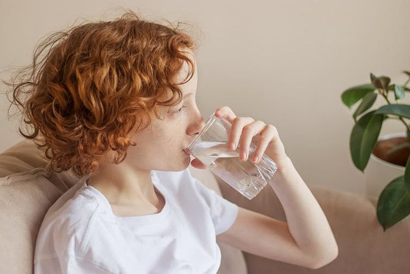 A teenage girl with flu drinks a glass of water