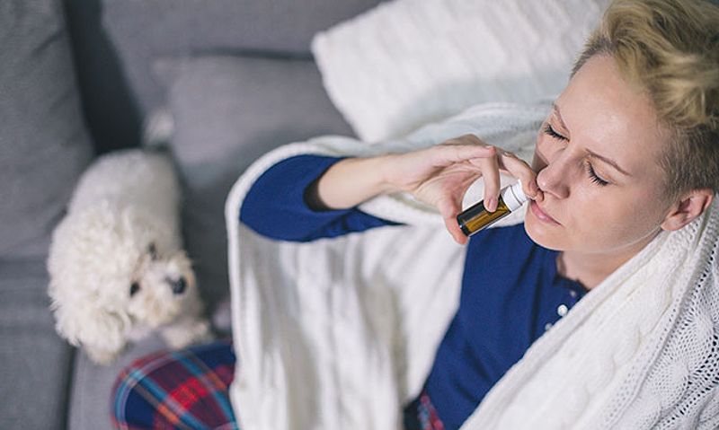 A woman using nasal spray to relieve sinus pressure while sitting on the couch with her dog